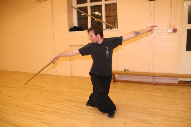 A student performs a staff form with arms outstretched