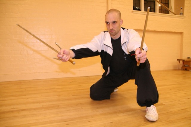An instructor crouched low holding two sticks