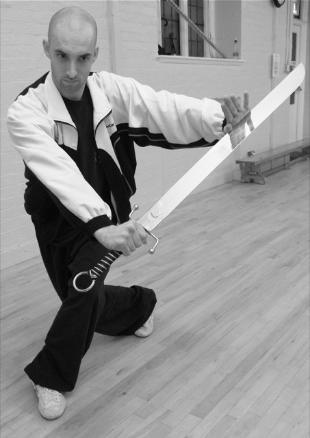 An instructor in a low stance holding a broadsword